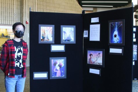 Senior Olive Guo stand next to his art exhibition in the auditorium lobby.